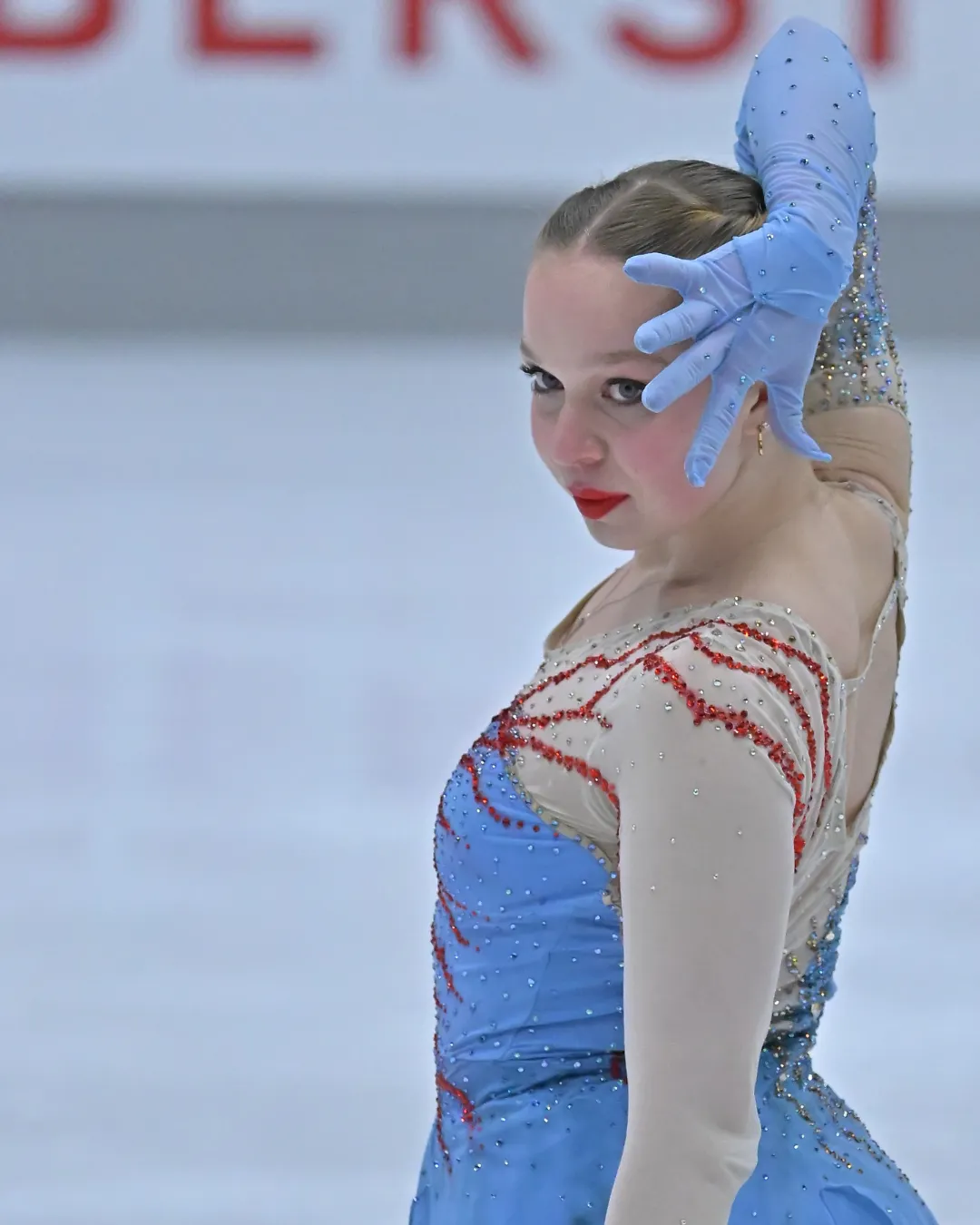 Eiskunstläuferin im blauen Kleid mit Handschuh vor dem Gesicht