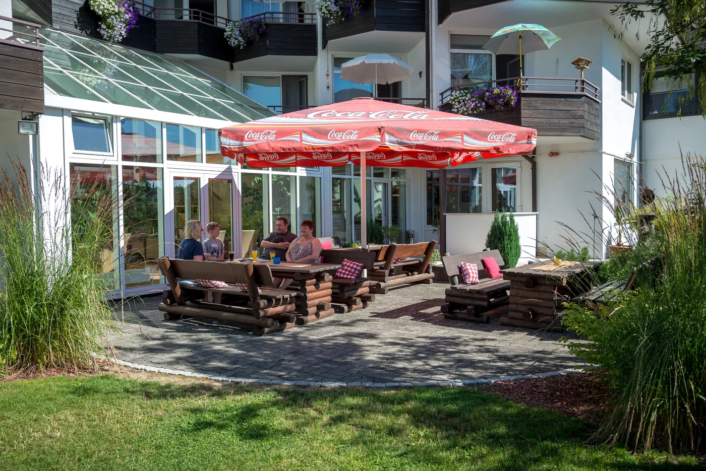 Gäste sitzen auf der sonnigen Terrasse vor dem Wintergarten