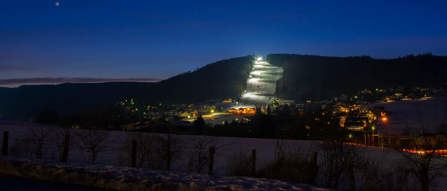 Beleuchtete Skipiste am Abend über dem verschneiten Upland
